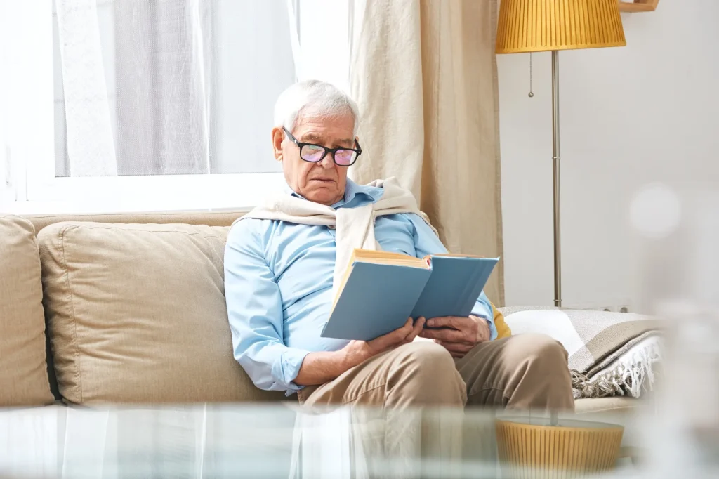 Senior man reading a book at home while experiencing blurry vision from cataracts